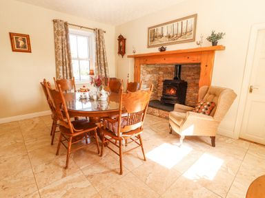 A dining room with a wooden table and chairs a stone fireplace with a wood stove and an armchair at Dromclough Farmhouse Dromclough near Listowel County Kerry