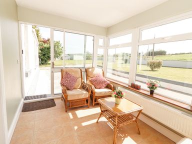 A sunroom with two cushioned chairs and a small table with flowers at Dromclough Farmhouse in Dromclough near Listowel County Kerry