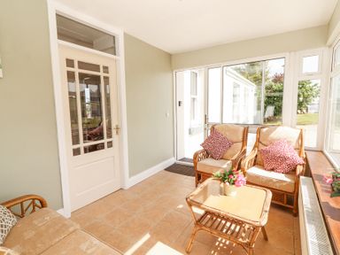 A sunroom with glass door two cushioned chairs and a table with a flower pot at Dromclough Farmhouse in Dromclough near Listowel County Kerry