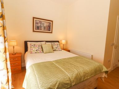 A bedroom with a double bed two bedside tables with lamps a framed picture on the wall and floral curtains at Dromclough Farmhouse in Dromclough near Listowel County Kerry