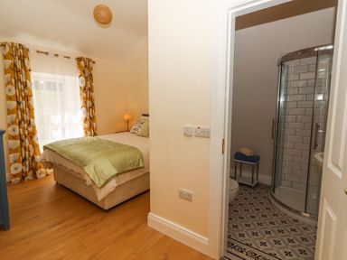 A bedroom with a bed green blanket and floral curtains next to a bathroom with a glass shower at Dromclough Farmhouse in Dromclough near Listowel County Kerry