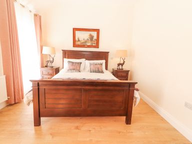A bedroom with a wooden bed frame two nightstands with lamps and curtains at Dromclough Farmhouse in Dromclough near Listowel County Kerry