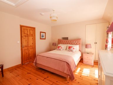 A bedroom with a double bed pink headboard two bedside tables with lamps wooden door and wooden floor at Dromclough Farmhouse in Dromclough near Listowel County Kerry