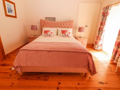 A bedroom with a bed with pink bedding and decorative pillows beside two bedside tables with lamps at Dromclough Farmhouse in Dromclough near Listowel County Kerry