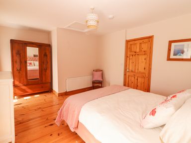 A bedroom with a wooden wardrobe a chair a wooden door and a bed with pink and white bedding at Dromclough Farmhouse in Dromclough near Listowel County Kerry