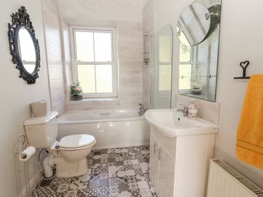 A bathroom with a toilet, bathtub, sink, round mirror, window, and orange towel at Dromclough Farmhouse in Dromclough near Listowel County Kerry