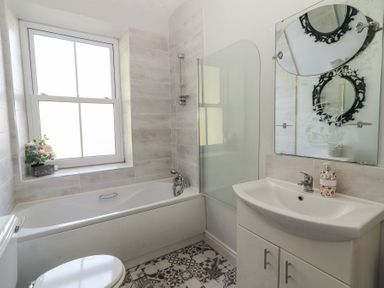 A bathroom with a bathtub, shower, sink with cabinet, toilet, window with flowers on the sill, and a mirror at Dromclough Farmhouse in Dromclough near Listowel County Kerry