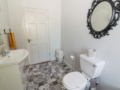 A bathroom with a white sink and cabinet a white toilet with a basket on top a patterned tiled floor and a decorative black framed mirror at Dromclough Farmhouse in Dromclough near Listowel County Kerry