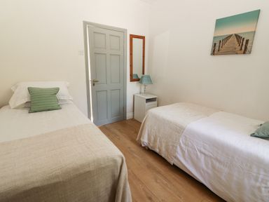 A bedroom with two single beds a gray door a nightstand with a lamp and a wall mirror and a picture of a pier at Dromclough Farmhouse in Dromclough near Listowel County Kerry