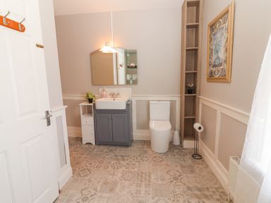 A bathroom with a sink vanity, toilet, mirror, small shelves, and patterned floor tiles at Dromclough Farmhouse in Dromclough near Listowel County Kerry