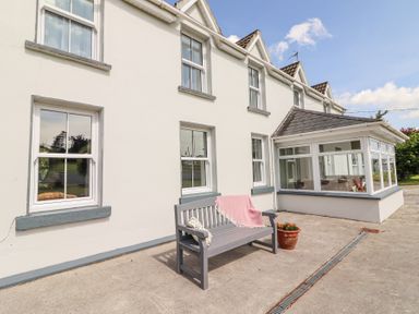 A white two-story house with a gray bench and a potted plant on a concrete patio at Dromclough Farmhouse in Dromclough near Listowel County Kerry
