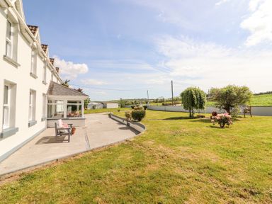 A house with a concrete patio and garden with shrubs and trees at Dromclough Farmhouse in Dromclough near Listowel County Kerry