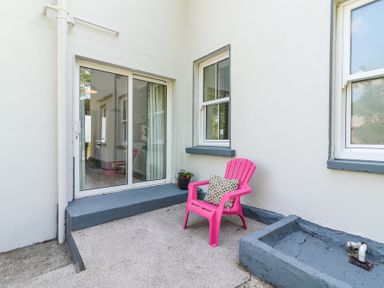 A small outdoor patio area with a pink chair and potted flowers outside white walls with sliding glass door and windows at Dromclough Farmhouse in Dromclough near Listowel County Kerry