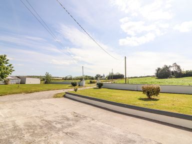 A concrete driveway with a grassy lawn and bushes along a gravel road and fields at Dromclough Farmhouse in Dromclough near Listowel County Kerry
