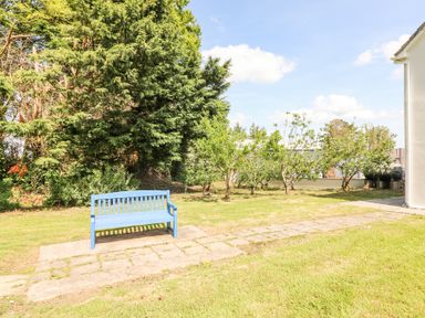 A blue bench on a paved area in a garden with trees and grass at Dromclough Farmhouse in Dromclough near Listowel County Kerry