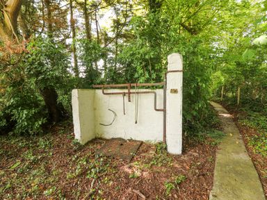 A small white concrete structure with metal bars and hooks in a wooded area near a narrow paved path at Dromclough Farmhouse in Dromclough near Listowel County Kerry