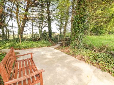 A wooden bench on a concrete path surrounded by trees and greenery at Dromclough Farmhouse in Dromclough near Listowel County Kerry