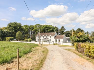 A farmhouse with a gravel driveway and trees surrounding the property at Dromclough Farmhouse in Dromclough near Listowel County Kerry