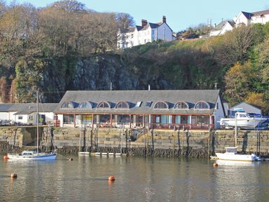 A waterfront building with arched windows and boats moored in the water at Fisherman Cove in Porthmadog
