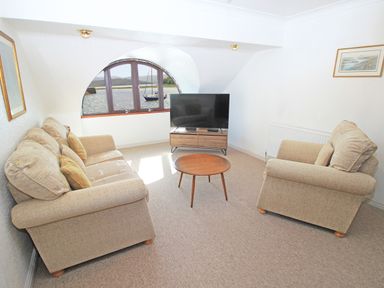 A living room with two beige sofas a round wooden coffee table a flat screen tv on a wooden stand and a window with a view of water at Fisherman Cove in Porthmadog