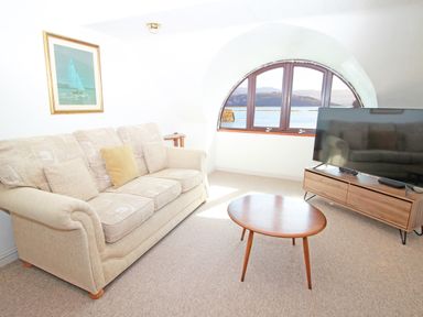 A living room with a sofa table tv and an arched window with a water view at Fisherman Cove in Porthmadog
