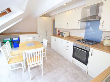 A kitchen with wooden countertops a dining table with four chairs and recycling bins at Fisherman Cove in Porthmadog