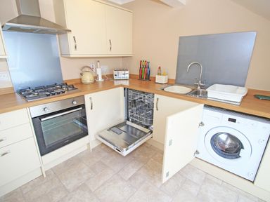 A kitchen with a gas stove oven dishwasher and washing machine with cream cabinets and wooden countertops at Fisherman Cove in Porthmadog