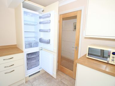 A kitchen with an open built in refrigerator and freezer a wooden door and a microwave on the counter at Fisherman Cove in Porthmadog