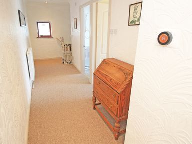 A hallway with a wooden chest of drawers a radiator a folding chair and a window at Fisherman Cove in Porthmadog
