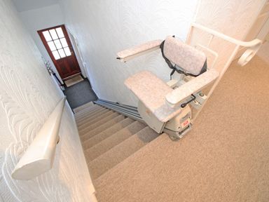 A stairwell with carpeted stairs and a stairlift chair installed at Fisherman Cove in Porthmadog
