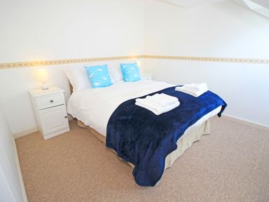 A bedroom with a double bed white bedding blue pillows blue blanket and two bedside tables with lamps at Fisherman Cove in Porthmadog