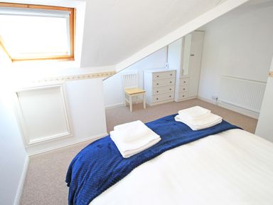 A bedroom with a bed folded towels a blue throw a white chair a white dresser and a skylight window at Fisherman Cove in Porthmadog