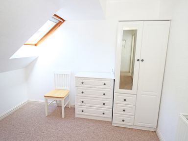 A small room with a white chair a white chest of drawers and a white wardrobe with a mirror at Fisherman Cove in Porthmadog
