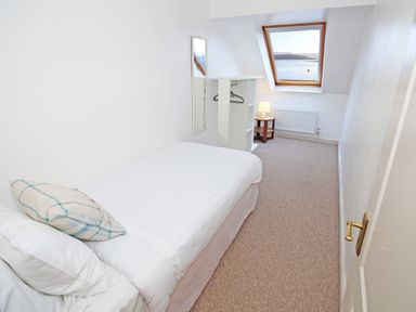 A bedroom with a single bed a window with a sea view a small table with a lamp and a wardrobe at Fisherman Cove in Porthmadog