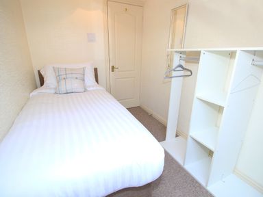 A small bedroom with a single bed a pillow a wall mirror and a white open wardrobe at Fisherman Cove in Porthmadog