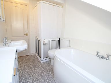 A bathroom with a white bathtub a toilet a shower with a curtain a white sink and a door at Fisherman Cove in Porthmadog
