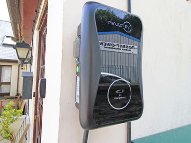 An electric vehicle charging station mounted on a white wall outside a building at Fisherman Cove in Porthmadog
