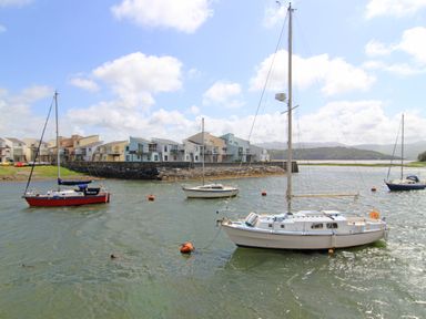 Sailboats anchored in a body of water with modern houses along the shoreline at Fisherman Cove in Porthmadog