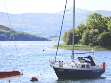 A sailboat named Moon Shadow anchored on a lake with hills and trees in the background at Fisherman Cove in Porthmadog