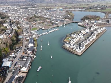 An aerial view of a harbor with boats docked and buildings along the waterfront at Fisherman Cove in Porthmadog
