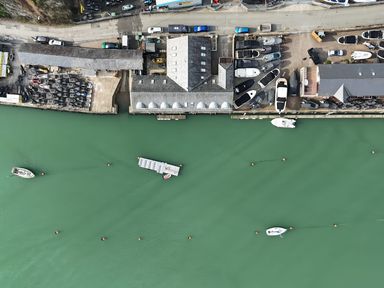 An aerial view of a marina with boats docked and buildings along the waterfront at Fisherman Cove in Porthmadog