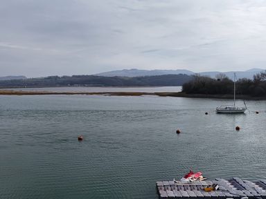 A body of water with a sailboat and a floating dock with equipment at Fisherman Cove in Porthmadog