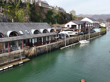 A waterfront scene with buildings along the water and boats docked at the pier at Fisherman Cove in Porthmadog