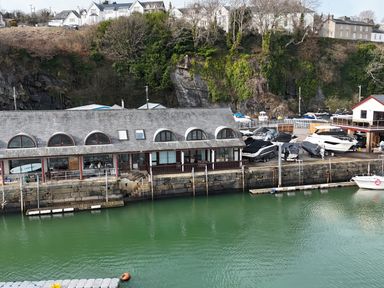 A waterfront building with boats docked and parked on the shore at Fisherman Cove in Porthmadog