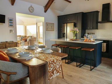 A kitchen with a dining table set for four and a kitchen island with four stools at Cuddfan in Llanfwrog near Bodedern