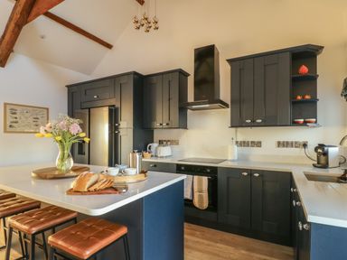 A kitchen with dark cabinets an island with stools a vase with flowers and bread on a cutting board at Cuddfan Llanfwrog near Bodedern