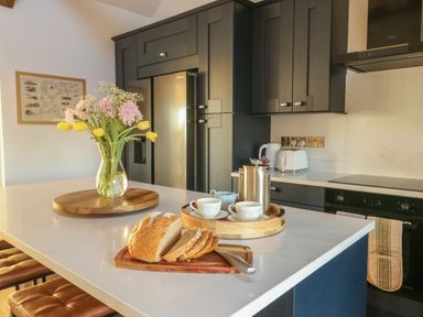 A kitchen with a marble countertop island featuring a vase of flowers sliced bread and a tray with coffee cups and a pot at Cuddfan in Llanfwrog near Bodedern