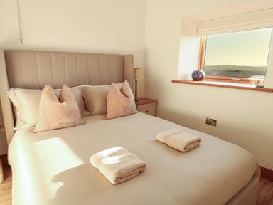 A bedroom with a double bed with pillows and towels and a window with a view at Cuddfan in Llanfwrog near Bodedern