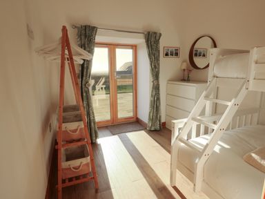 A bedroom with bunk beds a chest of drawers and a wooden clothes rack near glass doors with curtains at Cuddfan in Llanfwrog near Bodedern