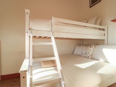 A bedroom with a white bunk bed and floral pillows at Cuddfan in Llanfwrog near Bodedern